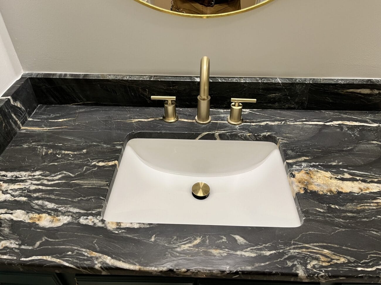 A bathroom sink with a rectangular white basin, gold faucet, and black marble countertop featuring white and gold veining.